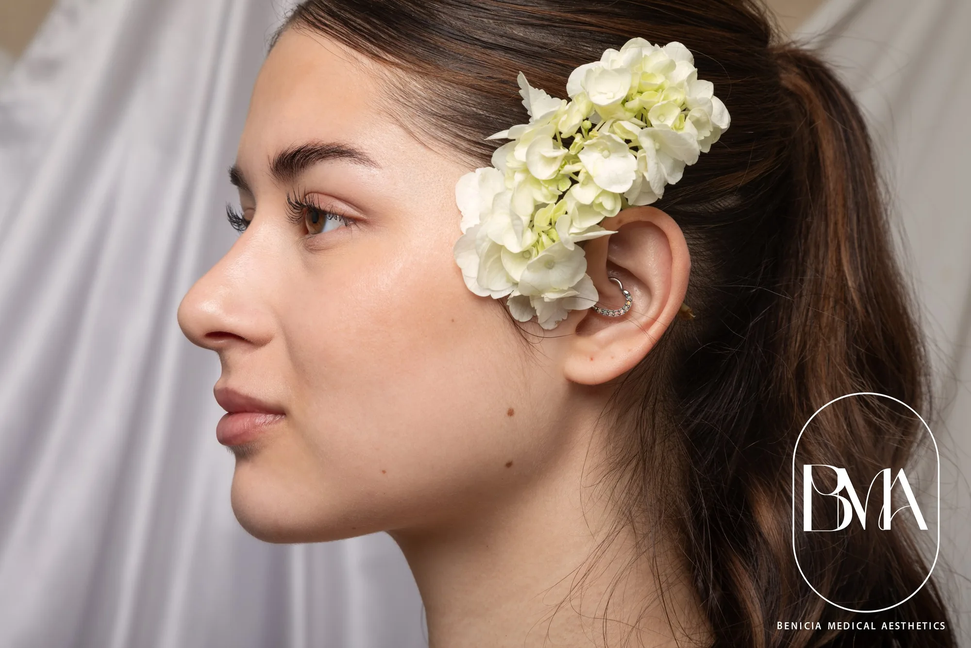 Woman in profile with white flowers in her hair beside the BMA monogram